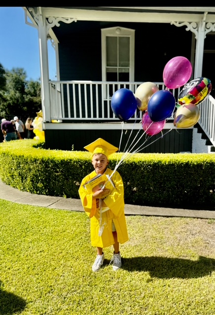little boy in yellow cap and gown with balloons