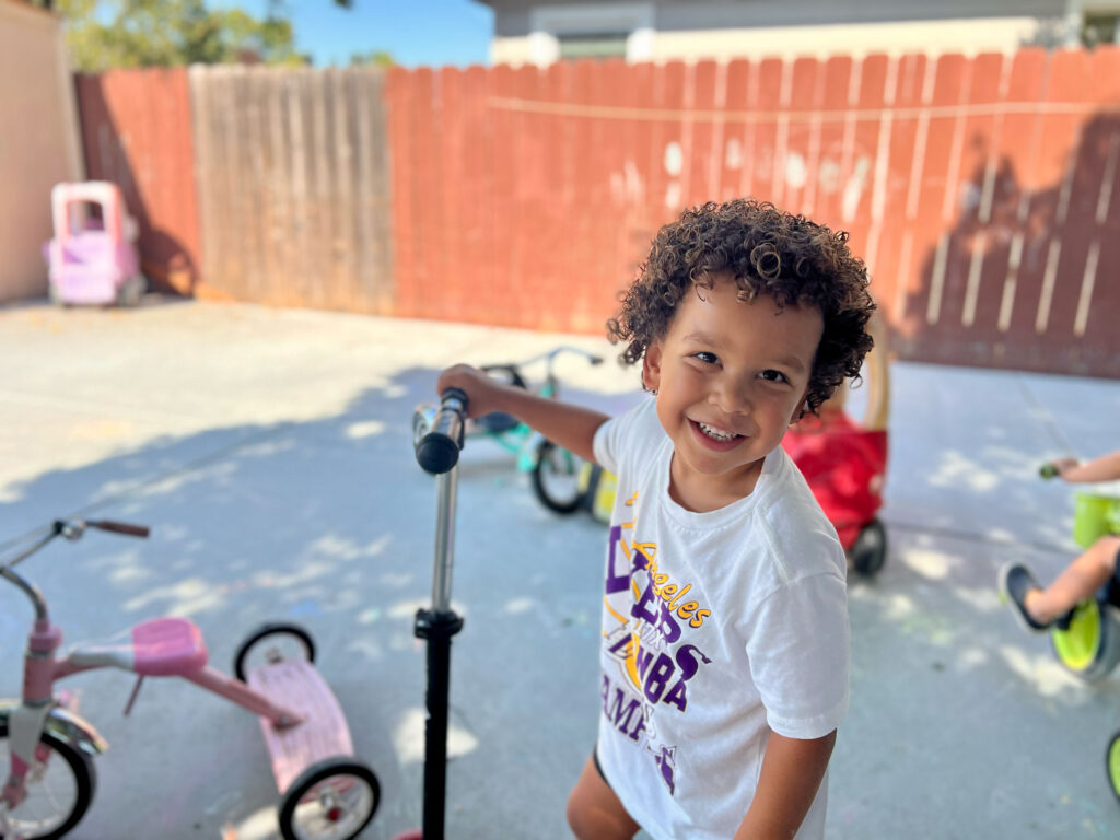 little boy riding a scooter looking at the camera smiling